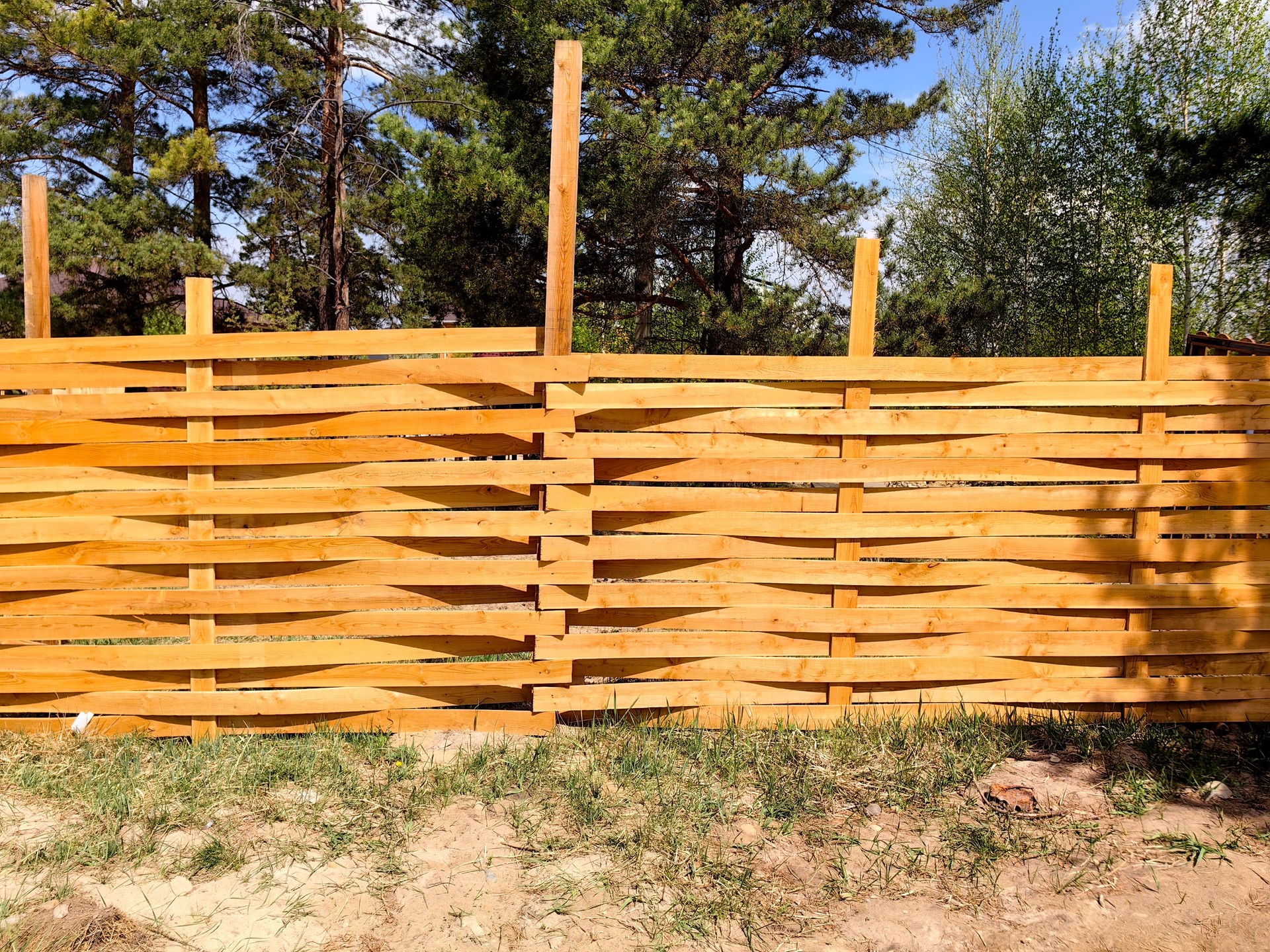 unique wooden fence design in sunny forest clearing with greenery nearby. closeup.